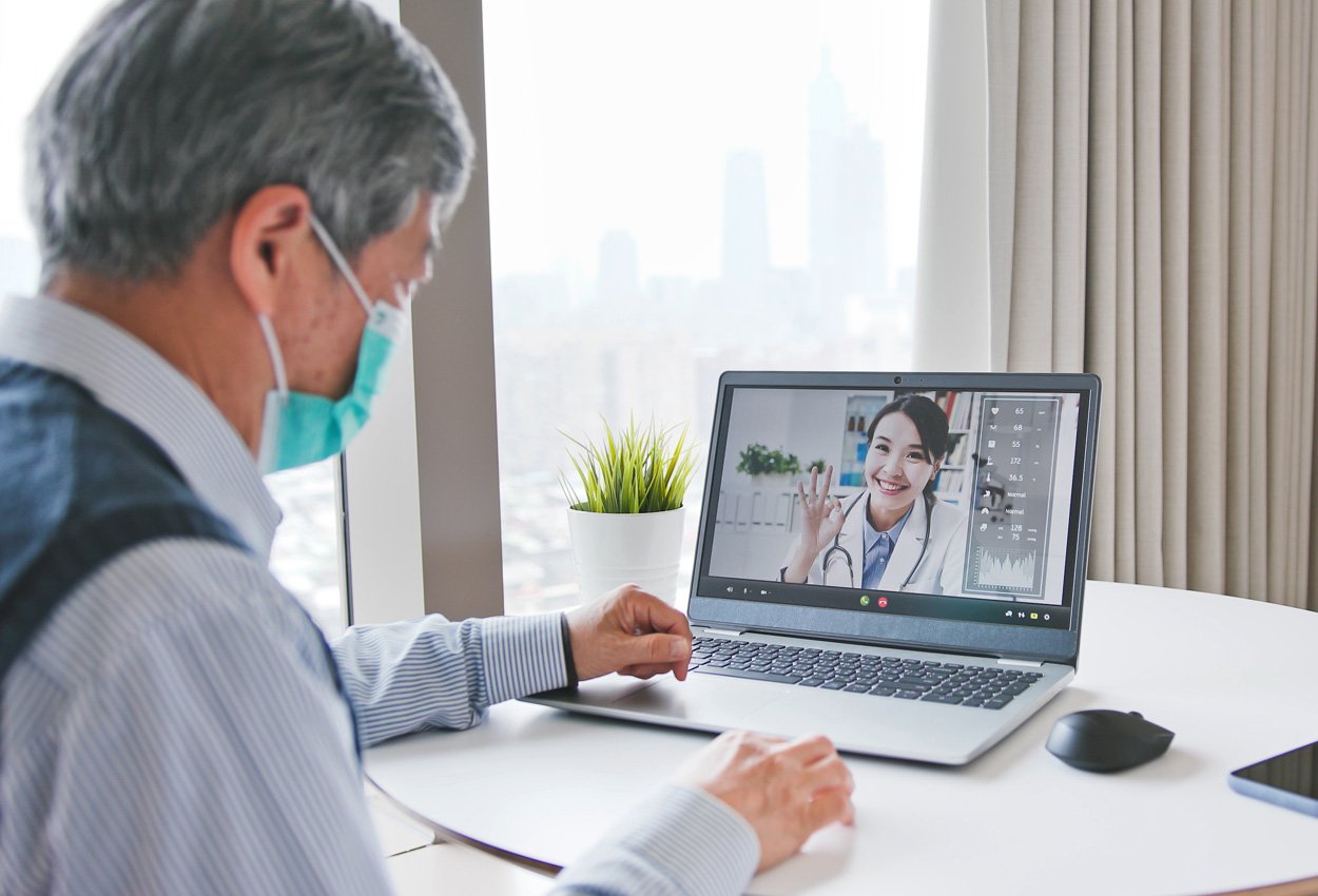 Older gentleman with COVID-19 mask on 'telehealth' call with doctor over laptop computer