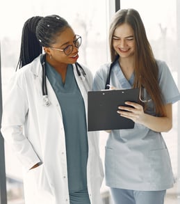 A doctor and nurse review paperwork together while smiling.