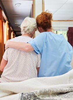 A nurse wrapping an arm around an elderly patient.