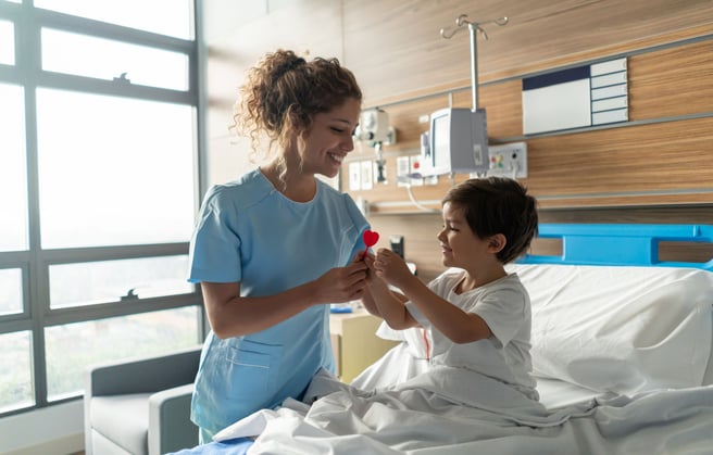 A nurse giving a pediatric patient a lollipop in a hospital bed.