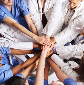 A group of healthcare professionals putting their hands together in the middle of a circle.