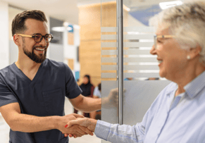 male imaging technician walking an older female patient out and shaking hands both happy and smiling