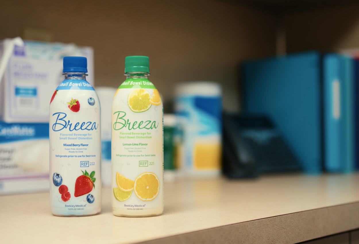 One bottle of mixed berry and one bottle of lemon lime Breeza on a medical desk with blurred box of gloves, phone, etc behind them