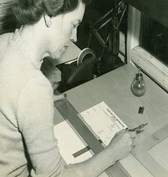 black and white photo of a lady at desk working on a charting sheet