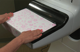 Hands smoothing a Bella Blankets protective coverlet, placed on the receptor plate during a mammogram