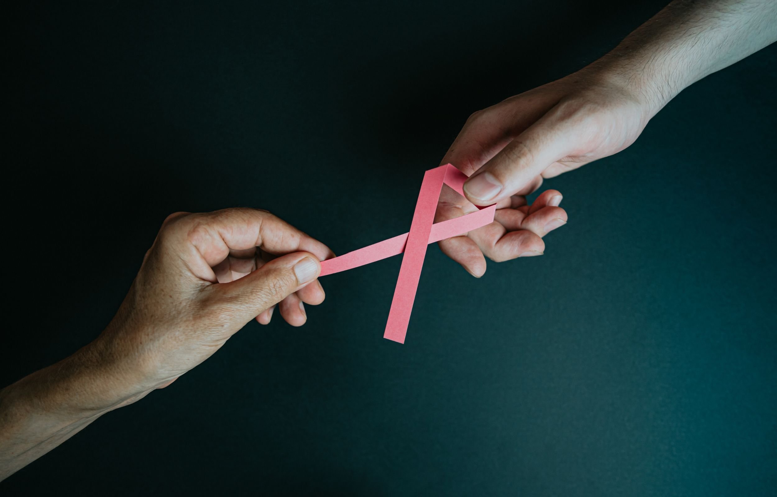 Two hands holding a pink breast cancer awareness ribbon.