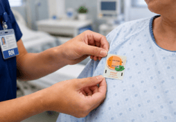 close up of nurse's hands putting an orange peppermint elequil aromatab on a patient gown near her should on chest