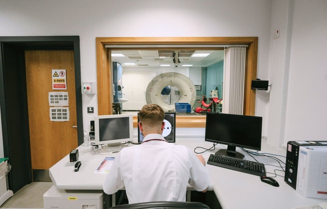 A radiologist looking at a screen with a CT machine in the background.
