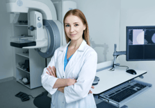 younger blonde female mammographer standing in front of machine and computer with arms crossed