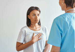 female african american patient with hand to her chest with a nervous look, talking to tech whose back is to the camera
