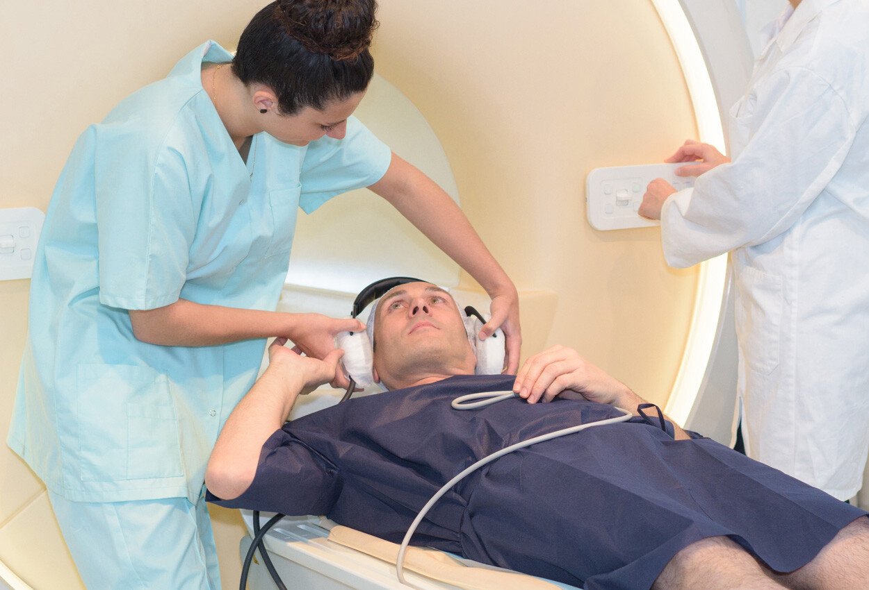 Patient undergoing an MRI procedure and appears a bit anxious. Technician applying ear protection to the patient in a comforting manner.