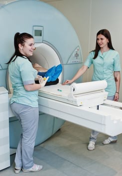 Two radiology technologists next to a patient on a MRI machine.