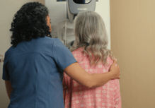 backs of tech and patient, tech helping position patient during mammogram