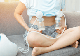 women with legs crossed sitting on a gray cough, not showing her head with light blue shirt on pumping breast milk